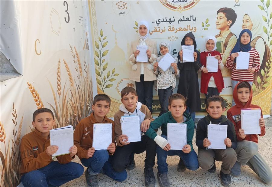 طلاب يعرضون دفاترهم أمام لوحة المدرسة